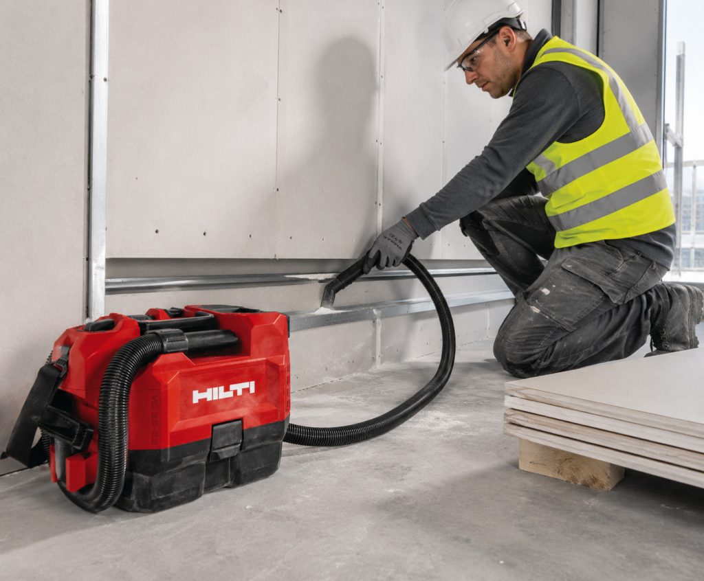 Akumulátorový stavebný vysávač Hilti VC 2D-22 pri čistení pracoviska počas montáže sadrokartónových konštrukcií a odsávania stavebného prachu v interiéri.