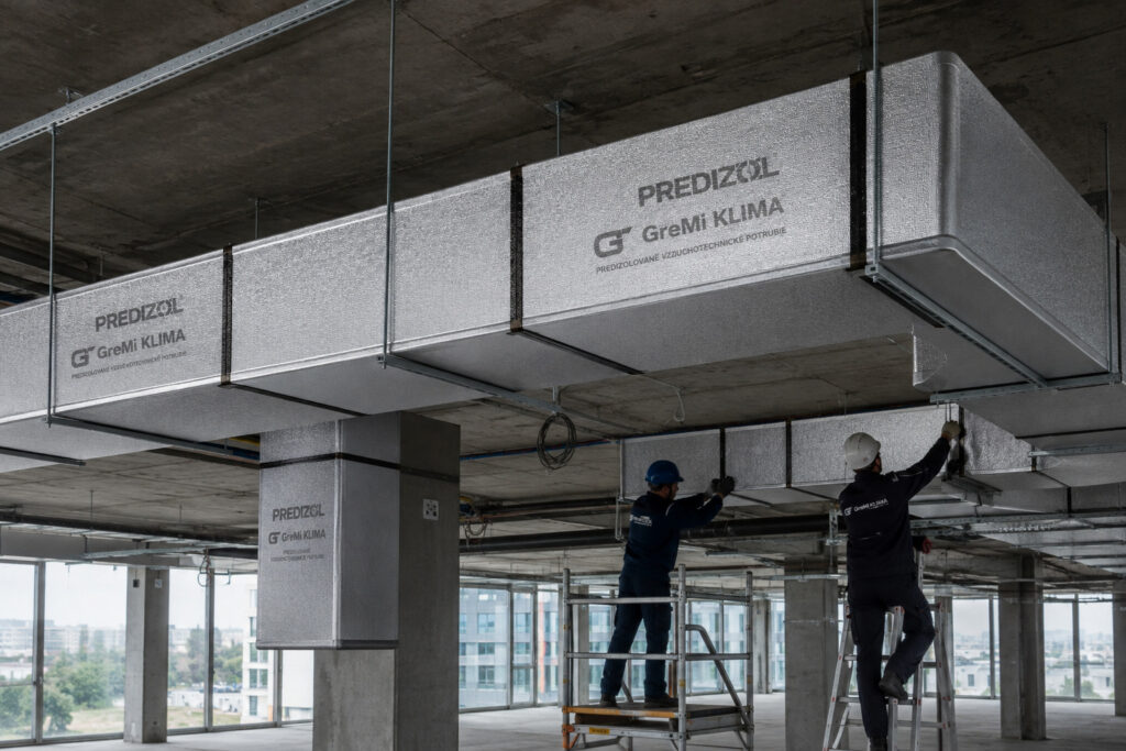 Predizolované vzduchotechnické potrubie PREDIZOL od GreMi KLIMA počas montáže v administratívnej budove s viditeľnými PIR panelmi, spojmi a závesným systémom.